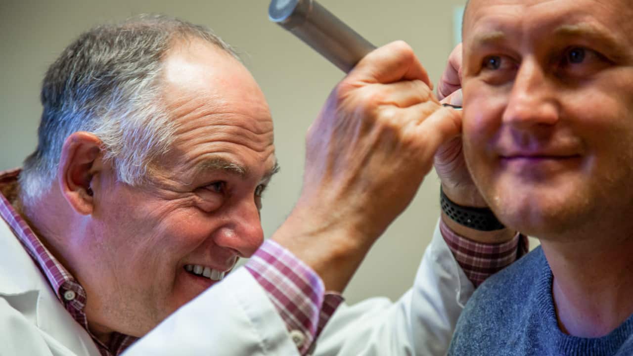 A physician inspects the inner ear of a male patient for a blog titled Why Men Over 30 Should Prioritize Their Annual Check-Ups by Richfield Medical Group
